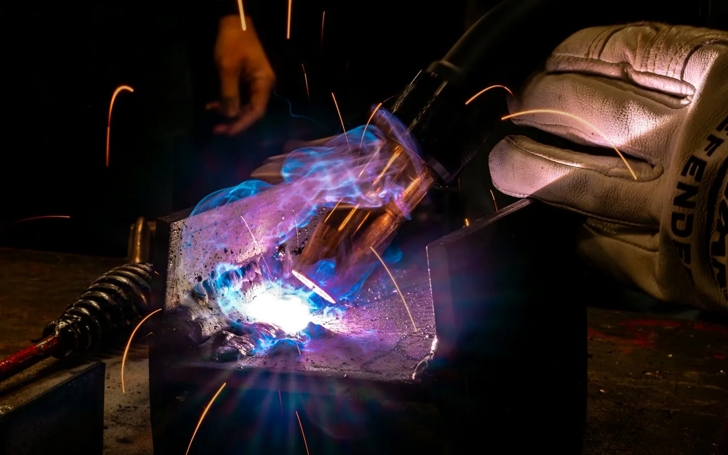 Mano guantata di un saldatore mentre l'arco accende le scintille sulla lamiera